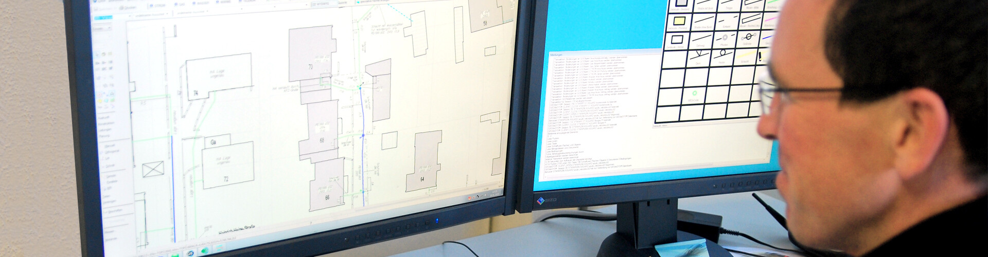 Ein Mann blickt auf zwei Computerbildschirme, auf denen Baupläne zu sehen sind.