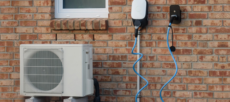 An einer Hauswand befindet sich eine Wärmepumpe, direkt daneben eine Wallbox für Elektrofahrzeuge.