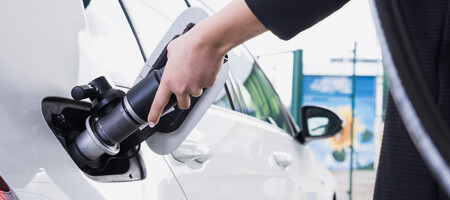 Eine Hand führt die Erdgas-Zapfpistole in die Tanköffnung, um das weiße Auto zu tanken.
