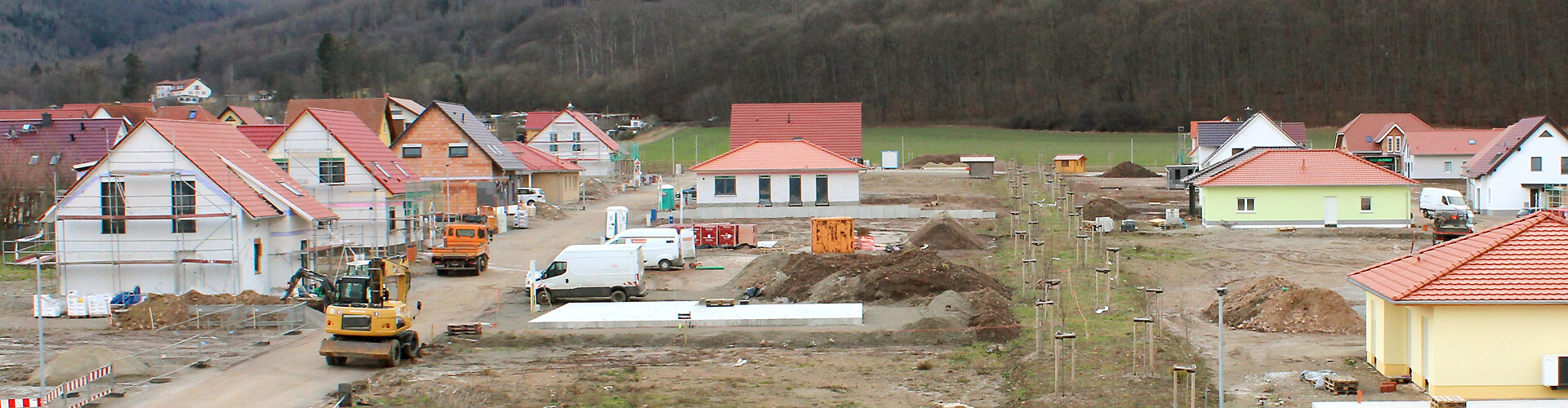 Ein Neubaugebiet mit zahlreichen Häusern wurde aus leicht erhöhter Perspektive von vorne aufgenommen. Zu sehen sind Gebäude mit Gerüsten sowie verschiedene Baufahrzeuge wie Bagger.