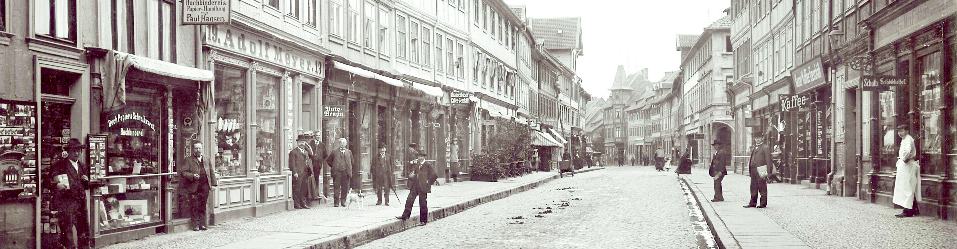 Schwarzweißfoto der Innenstadt von Wernigerode mit historischen Gebäuden, zahlreichen Geschäften mit großen Schaufenstern sowie Menschen in zeittypischer Kleidung mit Hüten.