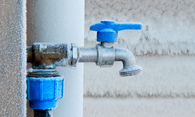 Ein vereister Außenwasserhahn, umgeben von ebenfalls mit Eis bedeckten Wänden.