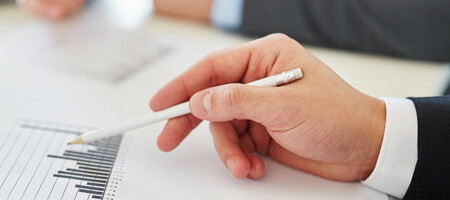 Eine Hand, die einen Bleistift hält, zeigt auf ein Balkendiagramm.