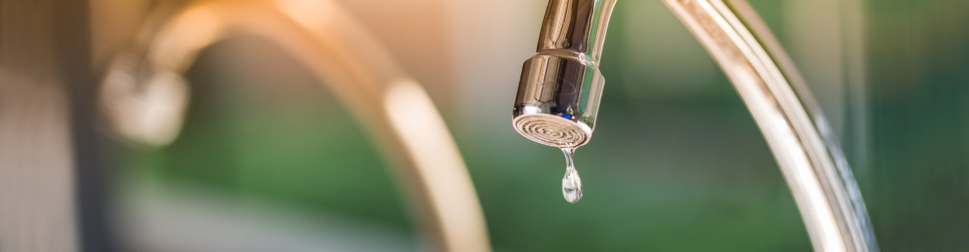 Ein tropfender Wasserhahn vor unscharfem Hintergrund.