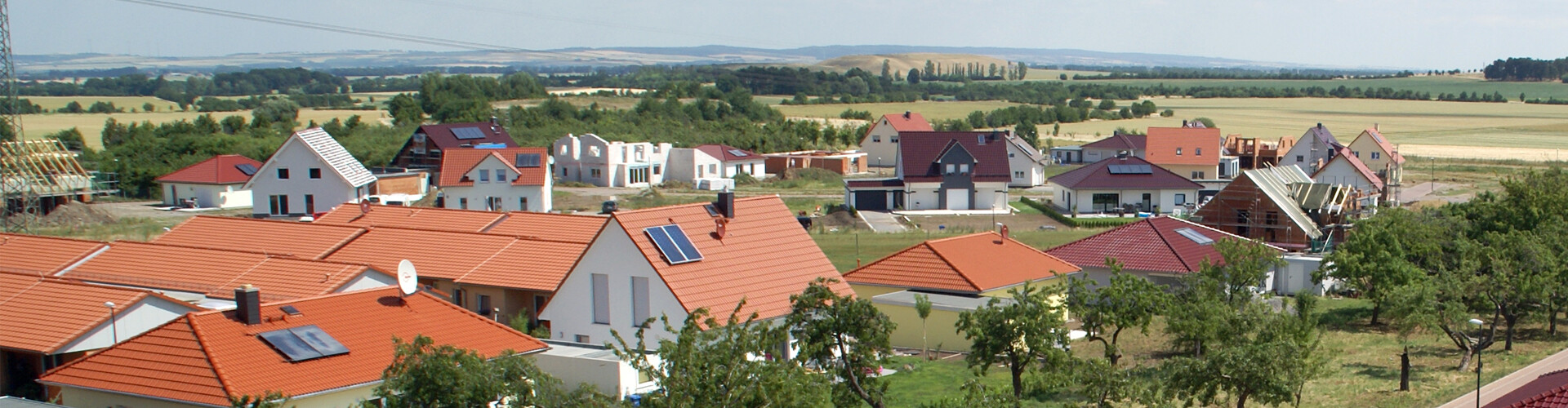 Viele neu gebaute Häuser sind aus der Vogelperspektive fotografiert, einige befinden sich noch im Bau. Das Bild zeigt ein Neubaugebiet, im Hintergrund erstrecken sich grüne Flächen.