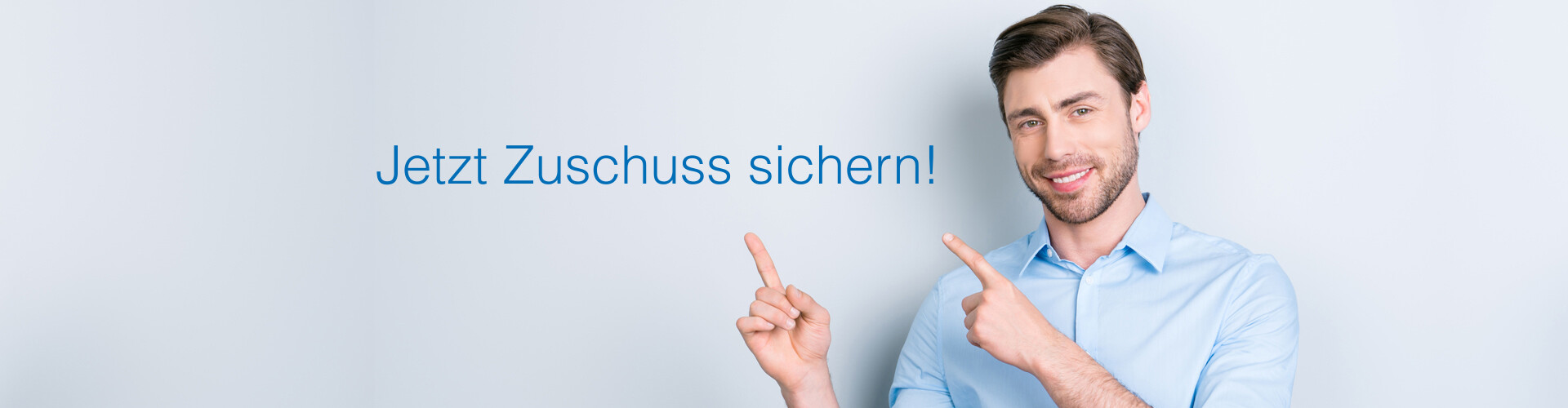Ein lächelnder Mann mit braunen Haaren und Bart trägt ein blaues Hemd. Er zeigt auf die Worte: „Zuschuss sichern!“.