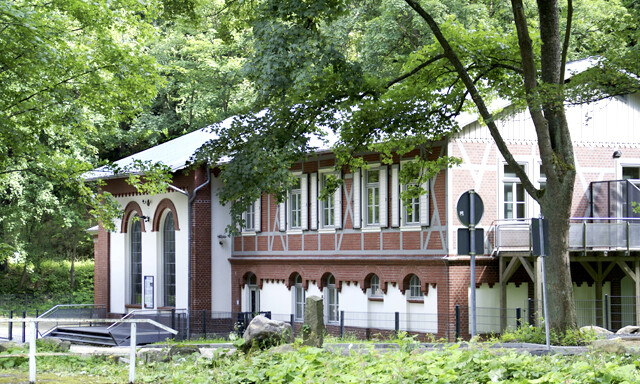 Abgebildet ist das Wasserkraftwerk „Steinerne Renne“. Die weiß-braune Fassade ist durch zahlreiche Fenster mit Fensterläden und Rundbögen geprägt. Außerdem verfügt das Gebäude über zwei Balkone. 