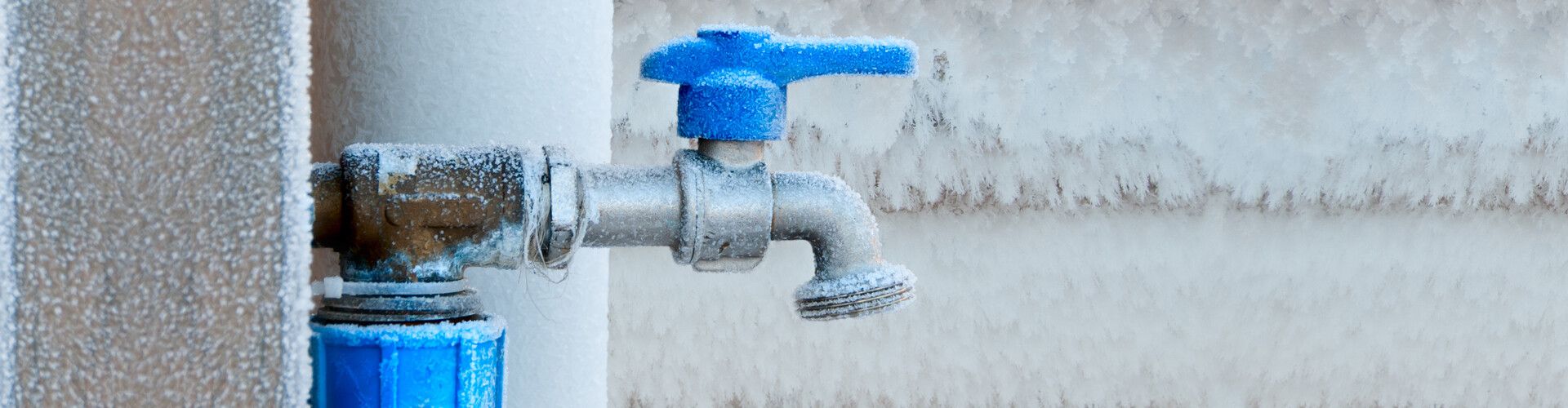 Ein vereister Außenwasserhahn, umgeben von ebenfalls mit Eis bedeckten Wänden.