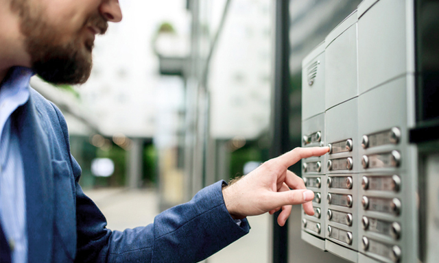 Mann drückt einen Klingelknopf und spricht über die Gegensprechanlage vor der Wohnung