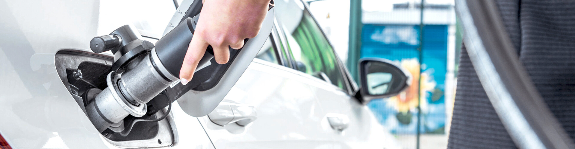 Eine Hand führt die Erdgas-Zapfpistole in die Tanköffnung, um das weiße Auto zu tanken.